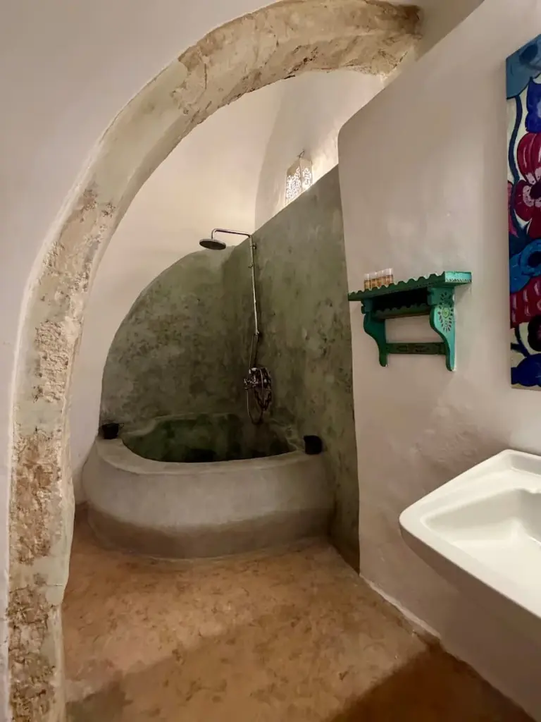 Bath and shower at Dar Dhiafa suite. The bath is in a white cave like bathroom with a vanity unit to th eleft