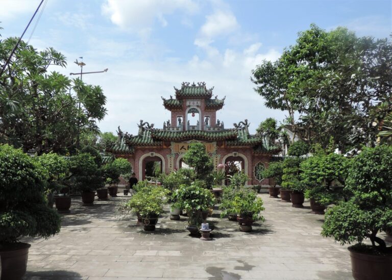 A temple in Hoi An, with 3 brick arches, which is covered covered in foliage adn plants