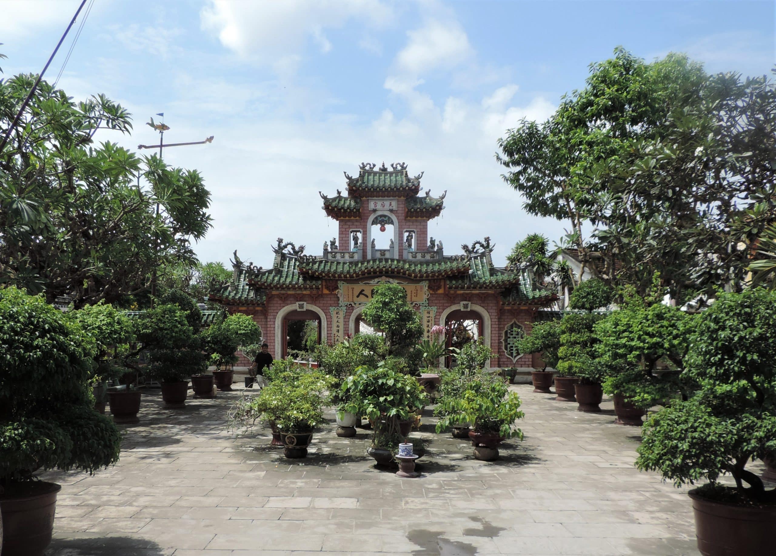 A temple in Hoi An, with 3 brick arches, which is covered covered in foliage adn plants